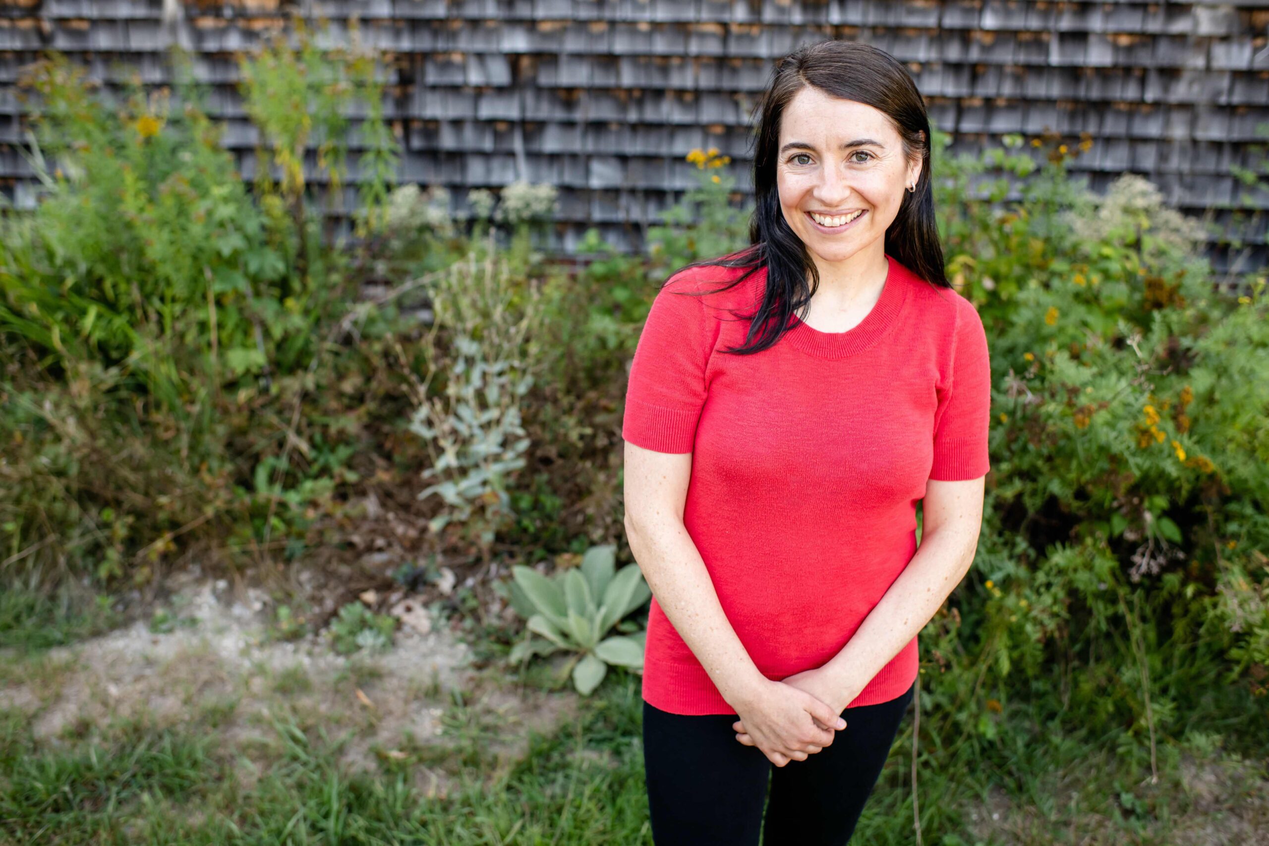 Couples therapist Leah Ottow, LCSW wearing a red shift and posing in front of a New England-Style shingled building