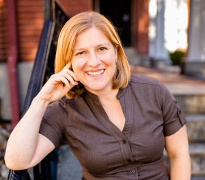 Hannah Curtis, LCSW owner of New Approaches wearing a brown dress, leaning against a rail